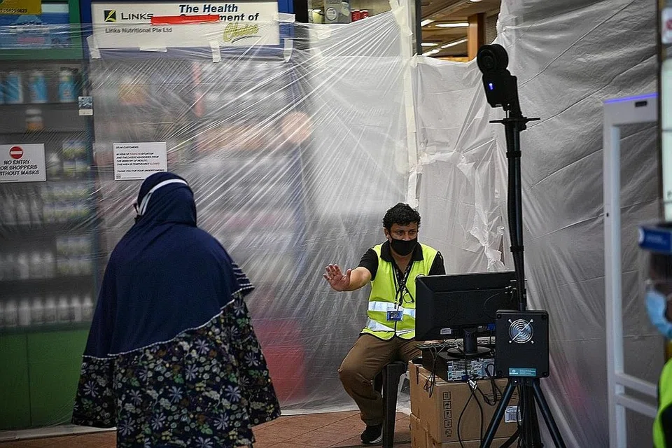PEMERIKSAAN SEBELUM BOLEH MASUK: Kakitangan memeriksa suhu badan pelanggan sebelum mereka memasuki Mustafa Centre kelmarin, hari kedua ia dibuka semula. Hanya bahagian pasar raya pusat beli-belah itu diizinkan dibuka mulai 6 Mei. - Foto BH oleh ARIFFIN JAMAR