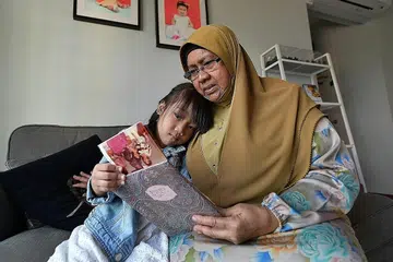LEBIH SELESA: Cik Jamnah kini mampu melihat sekelilingnya termasuk melihat album bersama cucunya, Adriana Hafiya Mohammad Aidil Adzahar, dengan lebih selesa selepas mendapatkan rawatan suntikan yang diperlukan di SNEC. - Foto BH oleh NG SOR LUAN