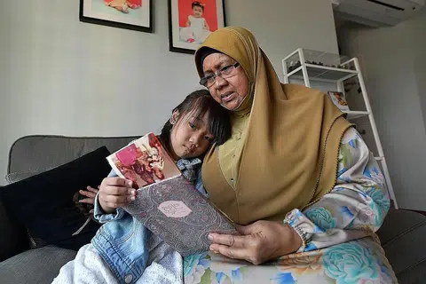 LEBIH SELESA: Cik Jamnah kini mampu melihat sekelilingnya termasuk melihat album bersama cucunya, Adriana Hafiya Mohammad Aidil Adzahar, dengan lebih selesa selepas mendapatkan rawatan suntikan yang diperlukan di SNEC. - Foto BH oleh NG SOR LUAN