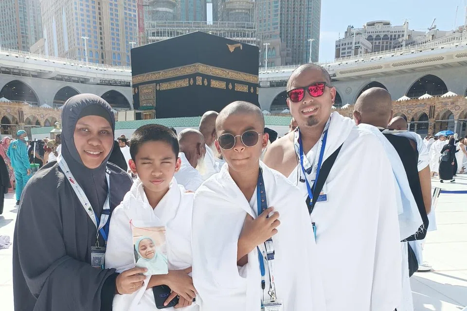 Encik Mohammed Ashraff Hussin bergambar bersama isteri, Cik Mardalina Mohamed Nossi, dan anak kembarnya Qayyim Fazhan Mohammed Ashraff (dua dari kiri) dan Qayyim Iylhan Mohammed Ashraff semasa menunaikan umrah pada Disember 2023. Cik Mardalina kelihatan memegang gambar Allahyarhamha Raisya Ufairah yang meninggal dunia akibat Covid-19.