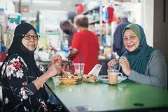 DAPAT SARAPAN BERSAMA: Cik Norimah Ngaji (kiri), dan adiknya Cik Norsimah Ngaji, bersarapan bersama di pusat penjaja di Pusat Pertukaran Bas Bedok semalam apabila larangan makan di luar dilonggarkan kepada kumpulan hanya dua orang yang diizin menjamu selera di luar. - Foto BH oleh HARITH MUSTAFFA