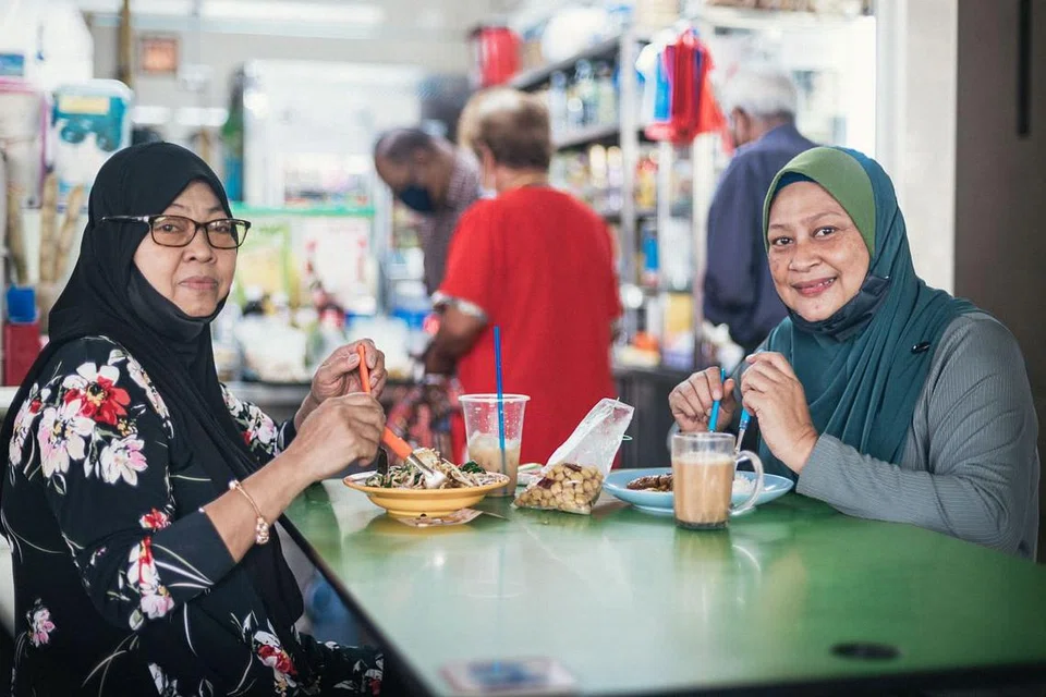DAPAT SARAPAN BERSAMA: Cik Norimah Ngaji (kiri), dan adiknya Cik Norsimah Ngaji, bersarapan bersama di pusat penjaja di Pusat Pertukaran Bas Bedok semalam apabila larangan makan di luar dilonggarkan kepada kumpulan hanya dua orang yang diizin menjamu selera di luar. - Foto BH oleh HARITH MUSTAFFA