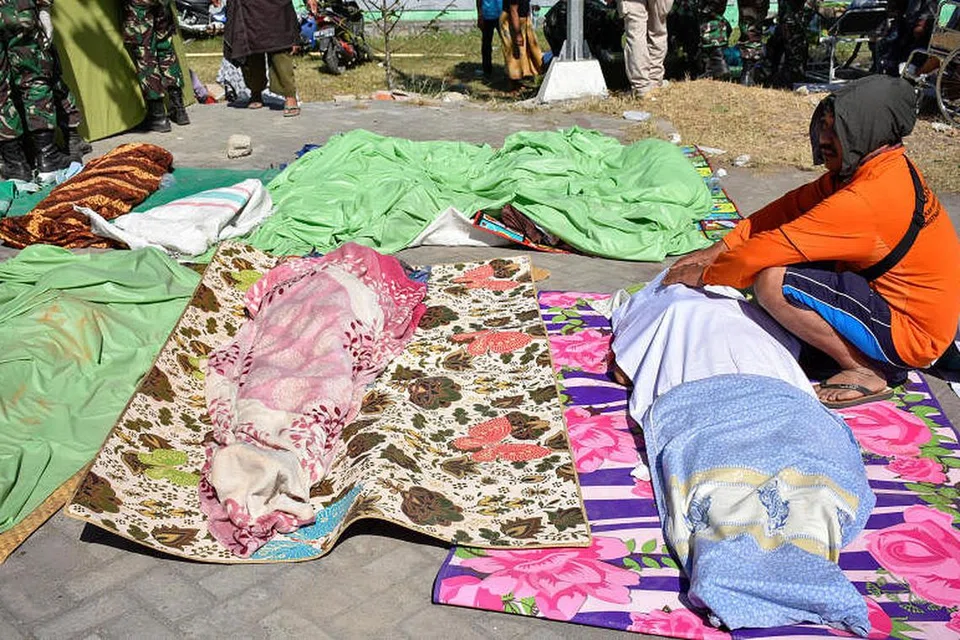Seorang lelaki duduk di sebelah mayat anggota keluarganya di Lombok. FOTO: Reuters
