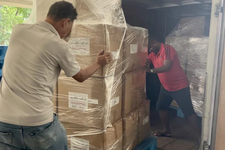 Pekerja kelihatan menolak beberapa kotak bekalan bantuan kemanusiaan yang telah dihantar ke Gaza ke dalam sebuah lori.