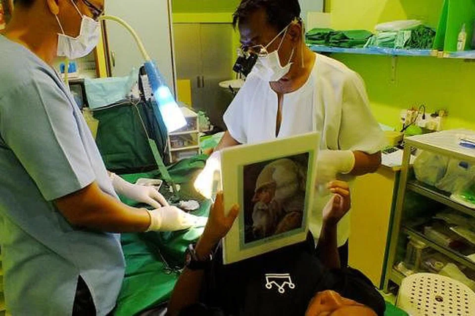 BORAK-BORAK UNTUK ALIHKAN PERHATIAN: Sambil jari ligat menjahit, Encik Alluwie (berbaju putih) bersama pembantunya menyuruh budak lelaki yang sedang dikhatankan berkongsi cerita di sebalik buku bergambar yang dipegangnya. - Foto SAINI SALLEH