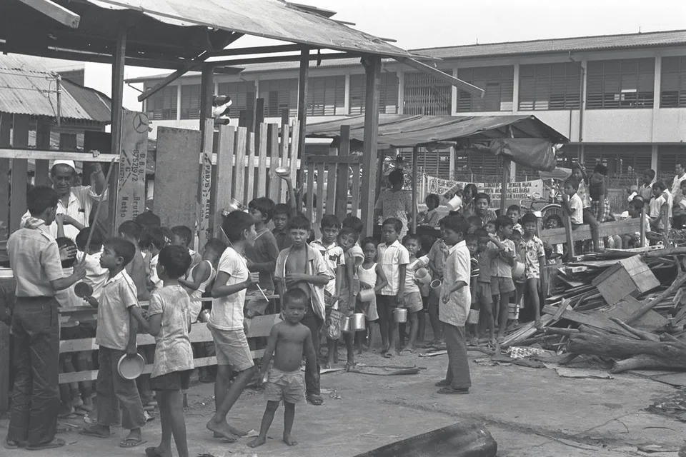 Berbekal belanga, mangkuk dan cawan, kanak-kanak beratur di pekarangan Masjid Aminah di Sims Avenue di Geylang pada 6 petang setiap hari untuk mengambil bubur yang diagih-agihkan masjid itu secara percuma, dalam gambar yang diambil pada awal tahun 70-an ini. Masjid itu kini sudah tiada, digantikan dengan Masjid Darul Aman di Jalan Eunos. Namun tradisi mengagihkan bubur kepada masyarakat ini terus dijalankan oleh masjid-masjid setempat sepanjang Ramadan.  