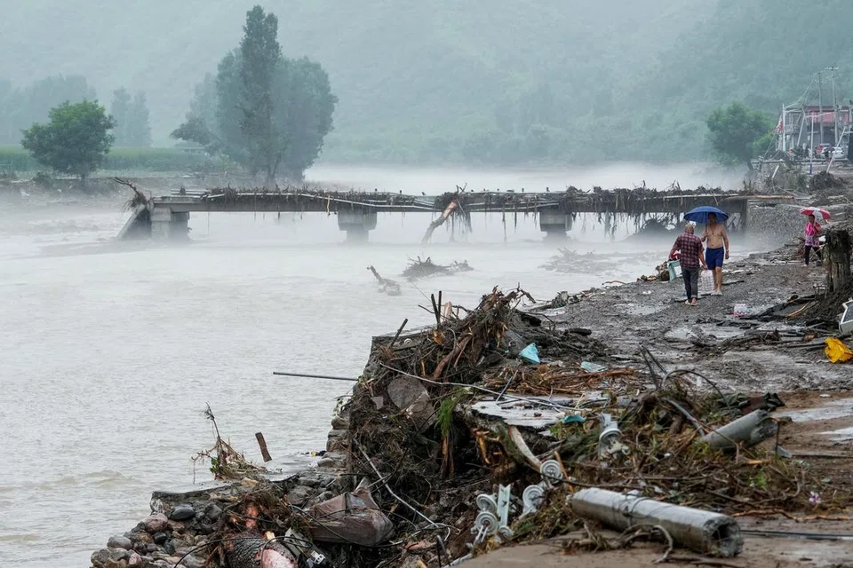 Orang ramai berjalan melewati sebuah jambatan yang rosak selepas hujan lebat menyebabkan banjir di kawasan itu, di daerah Huairou, Beijing, China pada 28 Julai 2025   