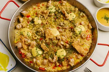 Paella con Pollo dimasak dengan ayam dan lada benggala, yang dihiasi dengan kulit ayam yang mempunyai perisa telur masin untuk kerangupan tekstur dalam setiap gigitan.