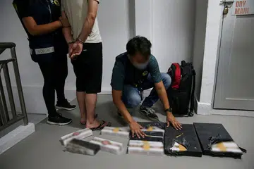 GAGAL SEMBUNYIKAN ROKOK: Seorang pegawai Kastam Singapura (gambar atas) memeriksa kandungan yang ditemui di dalam sebuah beg yang disembunyikan di tingkat 12 blok tempat tinggal kedua-dua suspek. Sebanyak 17 karton dan 14 paket rokok tidak dibayar cukai telah ditemui. - Foto BH oleh ZAIHAN MOHAMED YUSOF