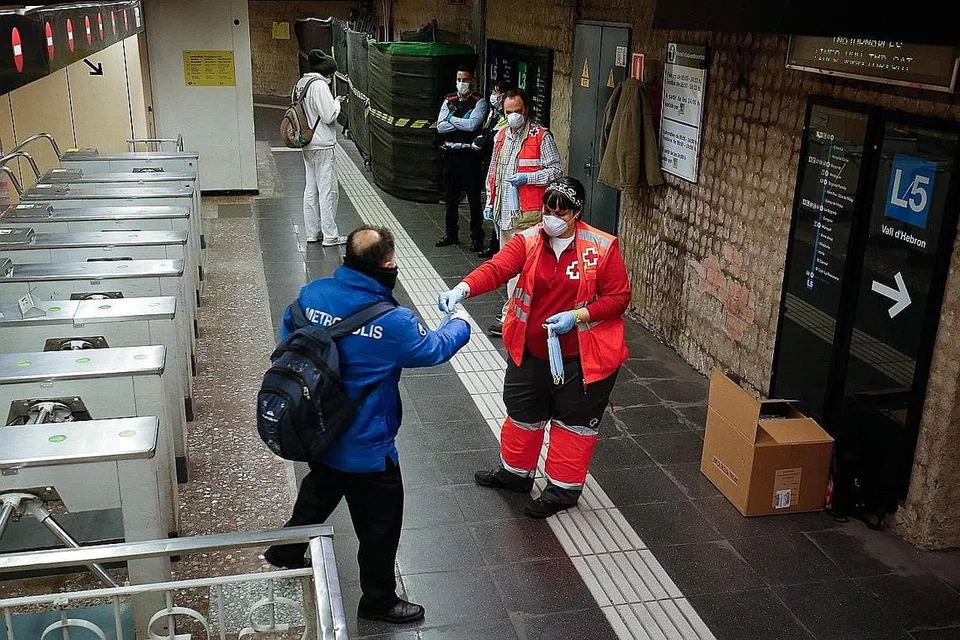 AGIH PELITUP: Sukarelawan Palang Merah mengagihkan pelitup kepada penumpang di stesen kereta api Sants di Barcelona, Sepanyol, pada 14 April lalu. - Foto AFP