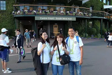 SAMBIL SELAM, MINUM AIR: Pelajar NYP, Cik Khoo (kiri) dan Cik Lim bersama pensyarah Encik Azhar bergambar di hadapan stadium berlangsungnya Kejohanan Wimbledon. Selain menyelesaikan projek industri politeknik itu, kededua pelajar itu ghairah dapat bertemu dengan beberapa bintang tenis dunia dengan lebih dekat lagi. - Foto NYP