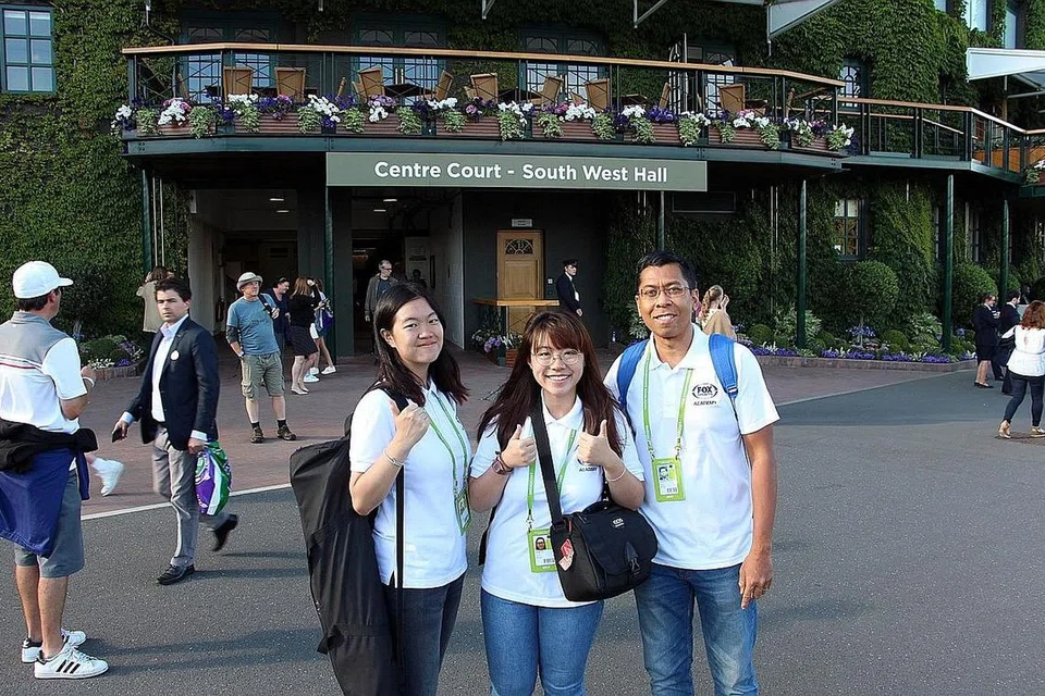 SAMBIL SELAM, MINUM AIR: Pelajar NYP, Cik Khoo (kiri) dan Cik Lim bersama pensyarah Encik Azhar bergambar di hadapan stadium berlangsungnya Kejohanan Wimbledon. Selain menyelesaikan projek industri politeknik itu, kededua pelajar itu ghairah dapat bertemu dengan beberapa bintang tenis dunia dengan lebih dekat lagi. - Foto NYP