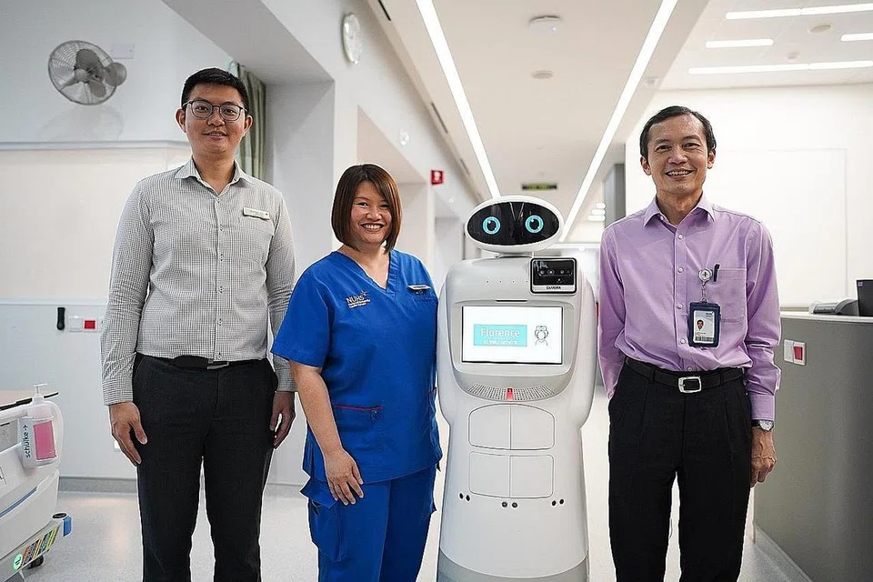 BERGAMBAR BERSAMA ROBOT: (Dari kiri) Encik Desmond Koh, Cik Doreen Heng, penolong pengarah kejururawatan di Hospital Alexandra, dan Profesor Lawrence Ho bersama robot yang boleh mengambil alih antara tugasan jururawat.