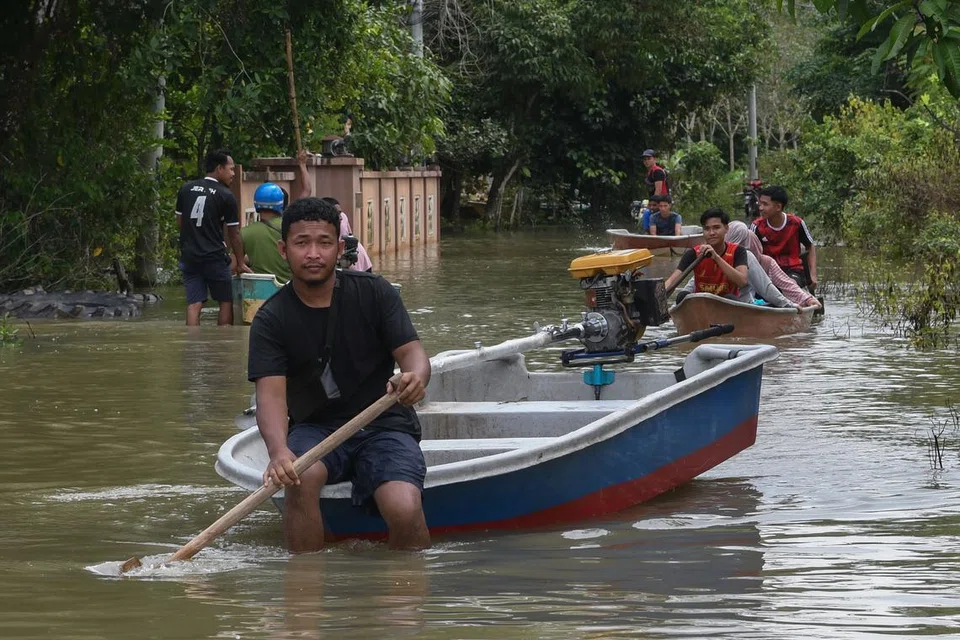 BANTU PINDAH PENDUDUK: Pemandu bot Encik Raihan Mohamad (kiri), 24 tahun, membantu memindahkan penduduk dari Kampung Serongga ke Pusat Pemindahan Sementara (PPS) Sekolah Kebangsaan Sri Kiambang berikutan kediaman mereka dilanda banjir pada 18 Disember.