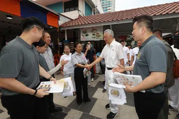 Bendahari Parti Bersatu Singapura (SUP), Cik Noraini Yunus (tiga dari kanan), bertembung dengan Menteri Kanan, Encik Lee Hsien Loong (dua dari kanan), di Pusat Makanan Ang Mo Kio pada 24 April. Cik Noraini sedang melakukan lawatan bertemu penduduk bersama anggota SUP lain, termasuk Encik Nigel Ng (kiri) dan Encik Andy Zhu (kanan). 