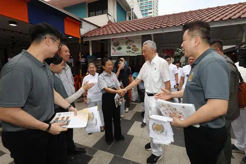 Bendahari Parti Bersatu Singapura (SUP), Cik Noraini Yunus (tiga dari kanan), bertembung dengan Menteri Kanan, Encik Lee Hsien Loong (dua dari kanan), di Pusat Makanan Ang Mo Kio pada 24 April. Cik Noraini sedang melakukan lawatan bertemu penduduk bersama anggota SUP lain, termasuk Encik Nigel Ng (kiri) dan Encik Andy Zhu (kanan). 