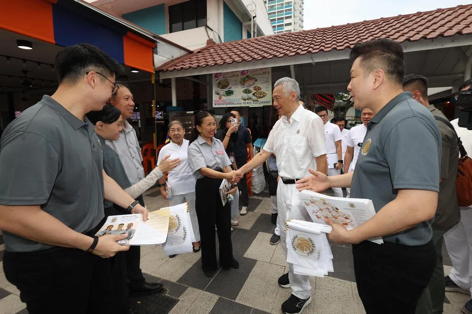 Bendahari Parti Bersatu Singapura (SUP), Cik Noraini Yunus (tiga dari kanan), bertembung dengan Menteri Kanan, Encik Lee Hsien Loong (dua dari kanan), di Pusat Makanan Ang Mo Kio pada 24 April. Cik Noraini sedang melakukan lawatan bertemu penduduk bersama anggota SUP lain, termasuk Encik Nigel Ng (kiri) dan Encik Andy Zhu (kanan). 