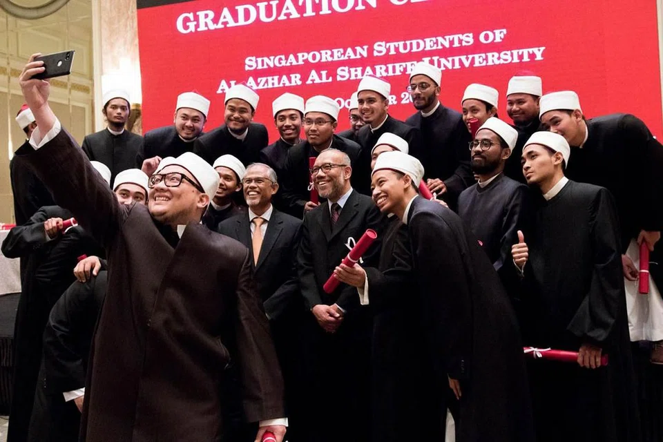 BUAT KENANGAN: Para siswazah Universiti Al-Azhar tidak melepaskan peluang berswafoto bersama Encik Masagos Zulkifli (tali leher oren) dan Dr Albakri Ahmad (tali leher coklat). - Foto MUIS