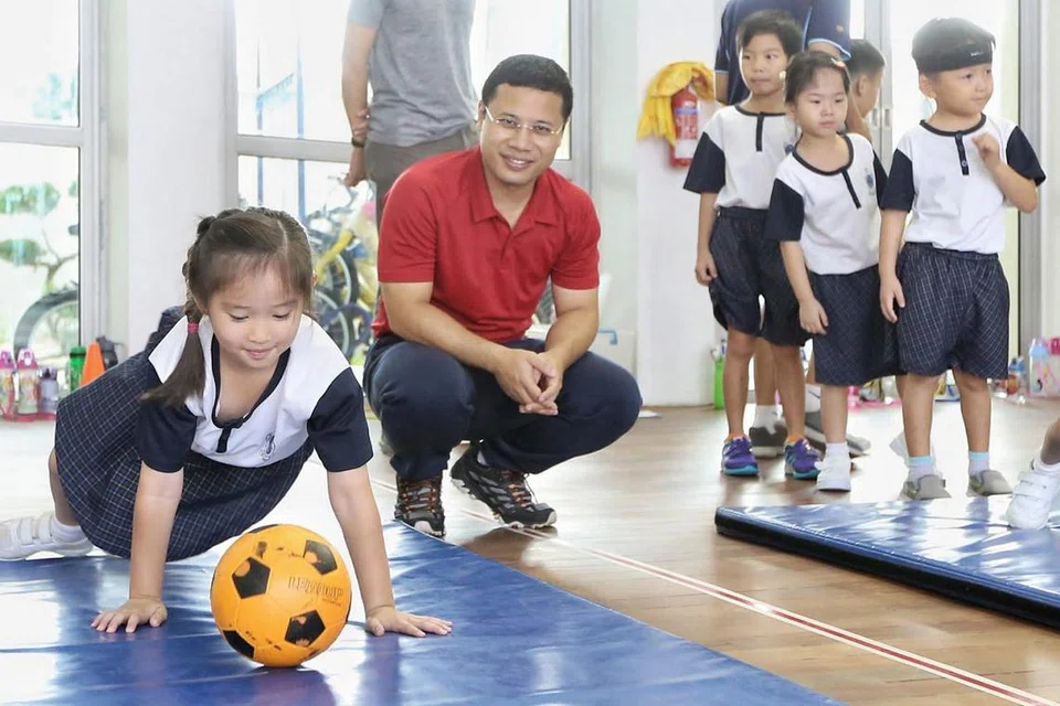 SERTAI SAMBUTAN HARI GURU: Encik Desmond Lee (berbaju merah) menyaksikan murid-murid di Prasekolah Canossaville yang mengambil bahagian dalam kegiatan sambutan Hari Guru mereka semalam. - Foto ZAOBAO