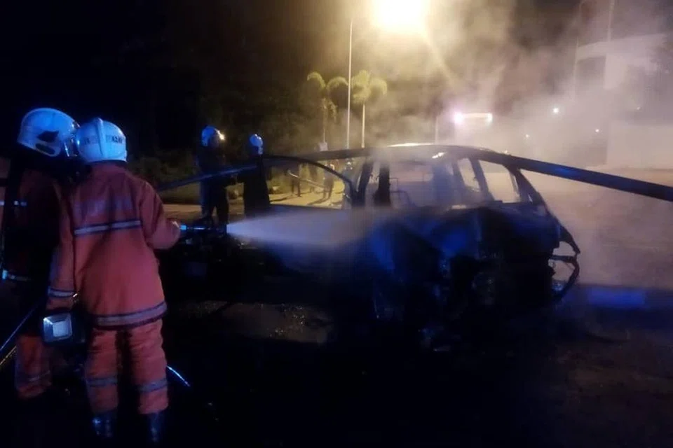 Pasukan bomba kelihatan menyembur air terhadap sebuah kereta di tempat kemalangan.