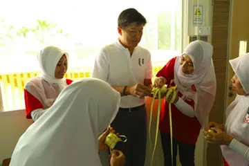 PAYAH TETAPI SERONOK: Encik Ng Chee Meng menyertai satu sesi bersama para relawan Pusat Pekerja Domestik baru-baru ini untuk belajar cara menganyam kelongsong ketupat. - Foto NTUC