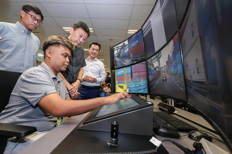 Encik Muhammad Sani Salim (duduk), seorang pemandu trak besar PSA, menunjukkan cara mengendali kenderaan kontena autonomi dari pusat kawalan PSA kepada Menteri Pengangkutan, Encik Chee Hong Tat (tiga dari kiri) semasa lawatannya ke Terminal Pasir Panjang PSA pada 16 Mei.