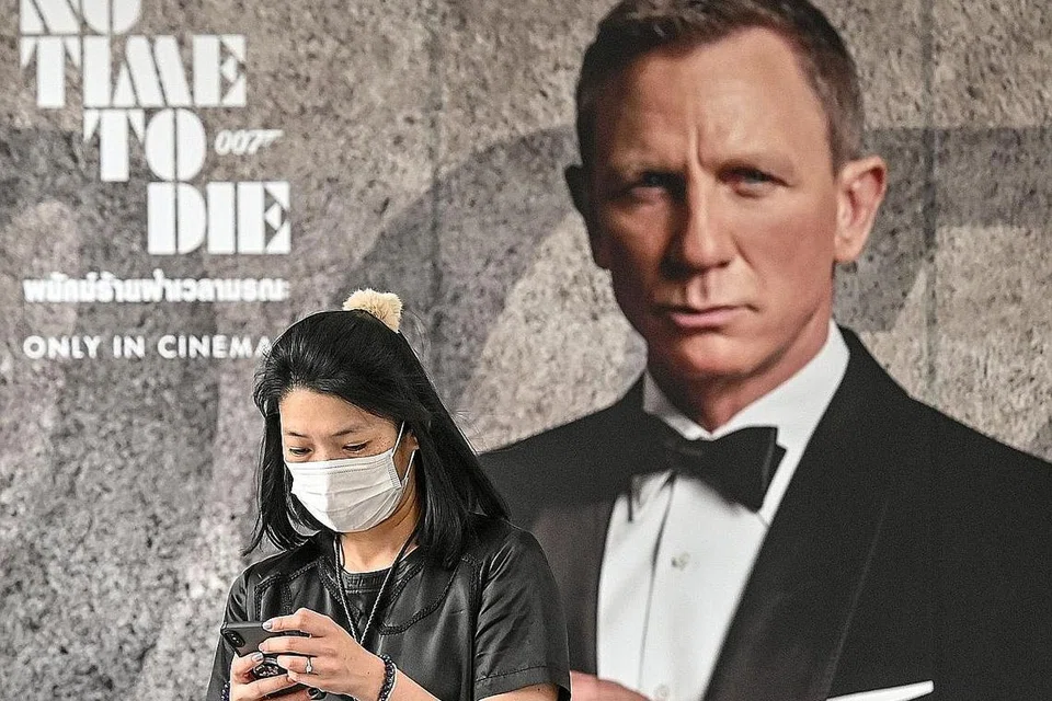 CEGAH SEBELUM KENA: Seorang wanita yang menggunakan pelitup bagi melindungi dirinya daripada dijangkiti Covid-19 berjalan lalu di hadapan poster filem terkini James Bond, No Time to Die di Bangkok. Penayangan filem itu kini ditangguhkan dan penglibatan dalam pesta filem dibatalkan. - Foto AFP