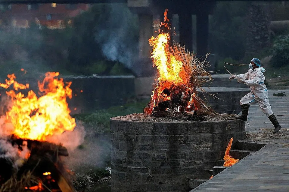 MEDAN BAKAR MAYAT: Sukarelawan dan ahli keluarga buat persiapan bakar mayat mangsa Covid-19 di kampung Giddenahalli, luar kawasan Bengaluru, India. (Atas) Seorang lelaki berpakaian alat pelindung diri (PPE) membakar sekujur mayat mangsa Covid-19 di pusat pembakaran mayat di Kathmandu, Nepal. - Foto-foto REUTERS