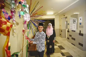HIASAN UNIK: Sebaik saja tetangga keluar dari lif Blok 117 Tampines Street 11 tingkat empat, mereka akan menikmati hiasan dua bunga manggar dan lampu pelita yang dihias oleh Encik Abdullah Abdul Rahim (kiri). Bersamanya ialah jiran Cik Rasida A Rahman yang gembira melihat hiasan Hari Raya tersebut dan berkata beliau boleh merasakan semangat Hari Raya. - Foto BH oleh DESMOND WEE