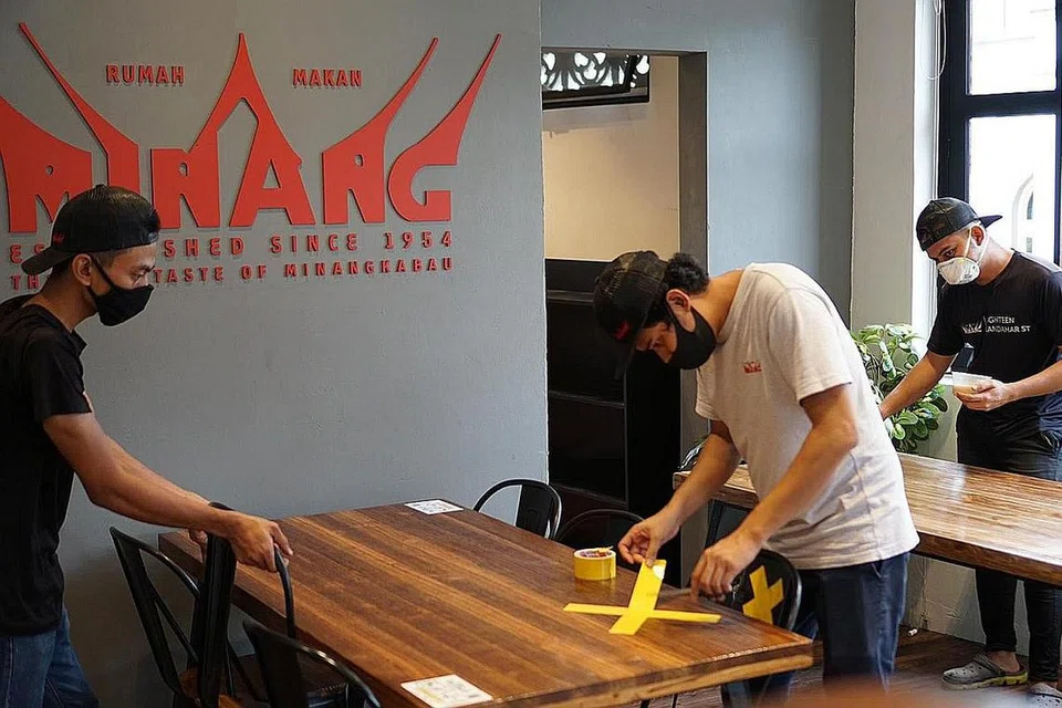 MEMBUAT PENYESUAIAN: Sebagai persiapan membuka semula perniagaan, Encik Hazmi Zin (tengah) telah mengambil beberapa langkah tambahan bagi menangani keprihatinan pelanggannya. Ini termasuk memastikan pelanggan membuat tempahan tempat sebelum menjamu selera, menyediakan perkakas pakai buang serta pelekat di meja bagi menjaga jarak selamat antara pelanggan. - Foto RUMAH MAKAN MINANG