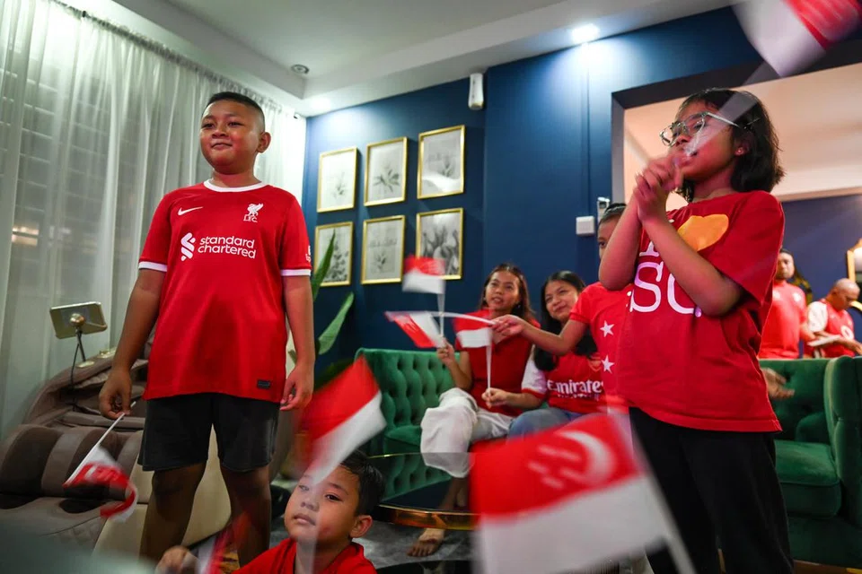 Kanak-kanak di sesi menonton anjuran Encik Muhammad Shahid Haron mengibarkan bendera Singapura sambil menikmati penstriman langsung Sambutan Kejiranan Hari Kebangsaan menerusi kaca televisyen. 