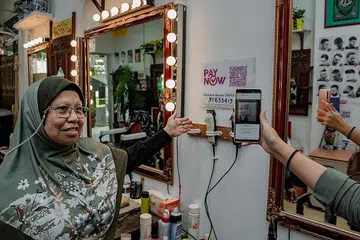 BAYAR SECARA DIGITAL: Pelanggan kedai gunting rambut Haji Osnam di Blok 239 Yishun Ring Road, yang dimiliki Cik Zainap Zainal Abidin bersama suami, boleh membayar menggunakan PayNow. Cik Zainap telah menyertai kursus untuk belajar tentang penggunaan perbankan digital, termasuk PayNow. - Foto BH oleh NUR DIYANA TAHA
