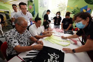 USAHA MENGHIJAU: Menteri Pembangunan Sosial dan Keluarga, Encik Masagos Zulkifli Masagos Mohamad (duduk, kiri) dan Anggota Parlimen GRC Jalan Besar, Dr Wan Rizal Wan Zakariah (duduk, dua dari kiri) belajar cara membuat beg beli-belah menggunakan kemeja-T terpakai di Blok 68 Geylang Bahru,pada 3 Disember. 