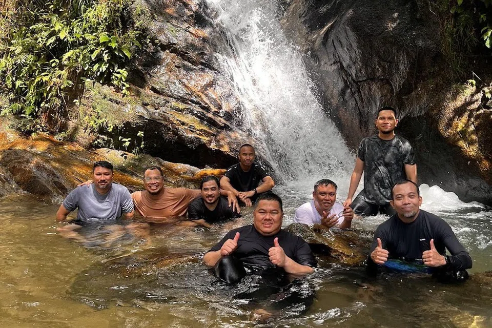 Encik Mohamad Firdaus Hasbullah (paling depan) dan Encik Mohammad Ridzuan Abdul Aziz (dua dari kanan) bermandi-manda di air terjun Kanching, di Rawang, Selangor, pada Januari 2025 bersama anggota Kelab Ayer Terjun yang lain.