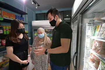 DAKAP TEKNOLOGI: Cik Aisha (tengah) bersama dua belia, Cik Tiffany Chia, 19 tahun (kiri) dan Encik Gordon Neo, 25 tahun (kanan), yang akan membantu membangun dan mengurus e-dagang perniagaannya menjual barang makanan beku halal, di bawah inisiatif iShop@Heartlands. - Foto BH oleh NG SOR LUAN