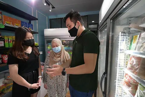 DAKAP TEKNOLOGI: Cik Aisha (tengah) bersama dua belia, Cik Tiffany Chia, 19 tahun (kiri) dan Encik Gordon Neo, 25 tahun (kanan), yang akan membantu membangun dan mengurus e-dagang perniagaannya menjual barang makanan beku halal, di bawah inisiatif iShop@Heartlands. - Foto BH oleh NG SOR LUAN