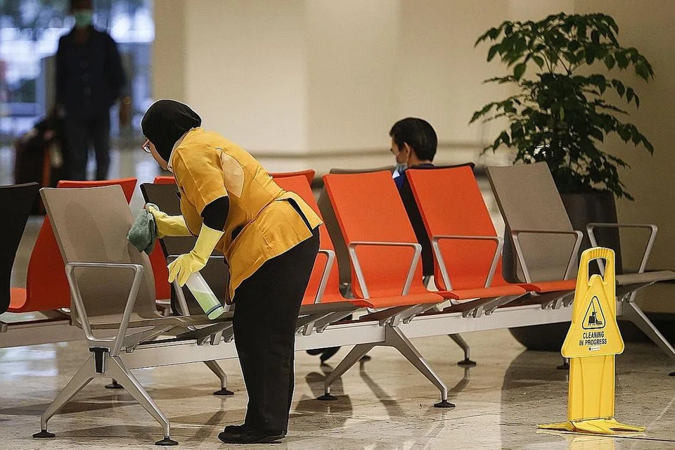 BERSIHKAN SEKITARAN: Seorang tukang bersih mengelap tempat duduk di dewan ketibaan di Lapangan Terbang Changi. - Foto EPA-EFE