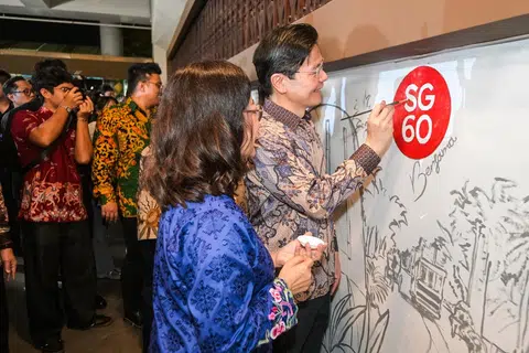 Perdana Menteri Encik Lawrence Wong (kanan) meletakkan lukisan pertama di Mural Masyarakat SG60, yang direka oleh pelukis tempatan, Salihin Jaafar, 35 tahun, yang lebih dikenali sebagai Fish Jaafar (tiga dari kanan). 