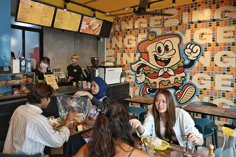 Suasana santai di kafe Binge yang menarik pelanggan daripada pelbagai latar belakang. Ikon maskot, Binge, dinamakan Benny yang melambangkan identiti santai dan mesra dilihat di dinding kafe itu. 