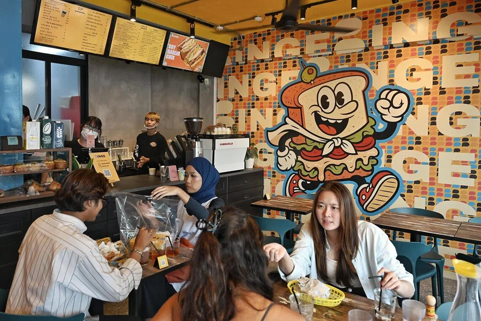 Suasana santai di kafe Binge yang menarik pelanggan daripada pelbagai latar belakang. Ikon maskot, Binge, dinamakan Benny yang melambangkan identiti santai dan mesra dilihat di dinding kafe itu. 