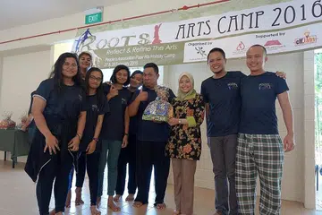 PELAJARI BAHASA DAN SENI MENERUSI PERKHEMAHAN: Anggota Parlimen (AP) GRC Jurong, Cik Rahayu Mahzam (baju bunga) menyampaikan hadiah kepada para peserta Perkhemahan Seni, Akar! yang diadakan awal tahun sambil diiringi Raja Hamzah (dua dari kanan). - Foto VARIASI PERFORMING ARTS