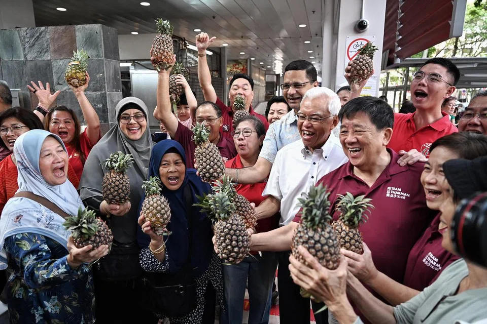 ‘HUAT AH!’: Para penyokong bakal Presiden Singapura, Encik Tharman Shanmugaratnam, melaungkan ‘huat ah!’ atau kemakmuran sambil memegang buah nanas yang diagihkan sementara menantikan ketibaan Encik Tharman di Pusat Penjaja Taman Jurong. 