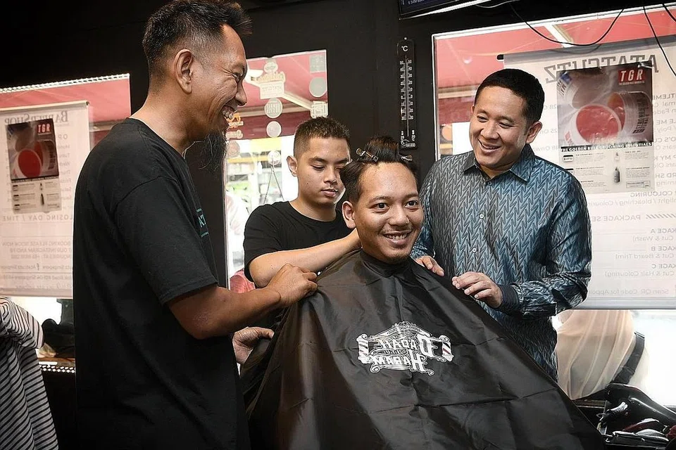 TEBAS SALAH FAHAM DADAH: Encik Amrin Amin (kanan) bersama tukang gunting rambut Atatzutz, (dari kiri) Encik Mohd Safri Anjopri dan Encik Muhd Khairul Ikhwan Jasmi, memakaikan mantel tukang gunting dengan slogan 'Dadah Itu Haram' pada pelanggan Muhd Zulhilmi Abu Bakar. - Foto BH oleh KHALID BABA