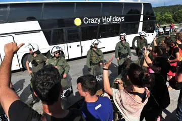 DIARAH PINDAH: Pendatang asing dan pelarian diminta berpindah menggunakan bas sedang sekumpulan pelarian lain mengadakan bantahan di depan barisan polis pencegah rusuhan di sempadan Greece-Macedonia semalam. - Foto AFP