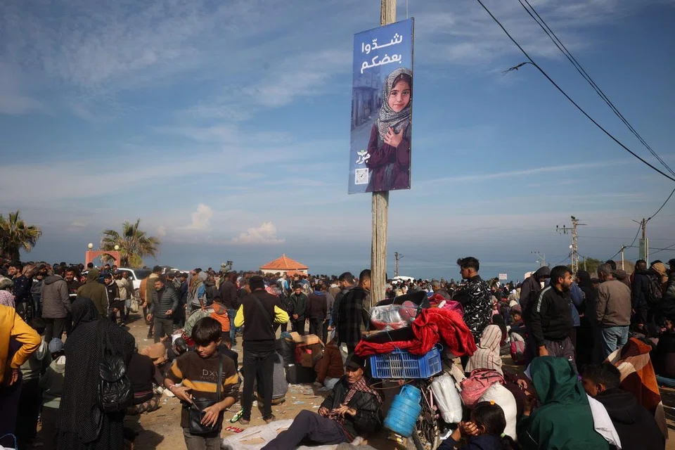 Sepanduk yang bertulis dalam bahasa Arab “saling menyokong” tergantung pada tiang ketika rakyat Palestin yang dipindahkan menunggu di sepanjang jalan Salah al-Din di Nuseirat, berhampiran koridor Netzarim yang disekat, untuk melintasi ke bahagian utara Jalur Gaza pada 26 Januari.