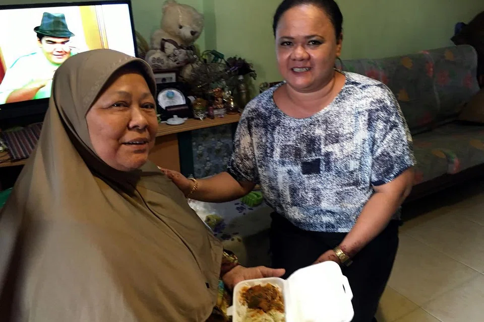 TIDAK PERLU MASAK: Cik Zainab (kiri) yang berkerusi roda, berterima kasih kepada angggota MAEC Kelab Masyarakat Boon Lay, Cik Haslina, yang membantu menghulurkan makanan percuma kepadanya di Boon Lay Drive. - Foto DEWANI ABBAS