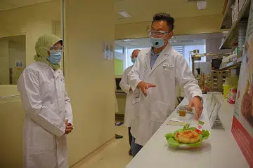 HASIL MAKANAN GUNA TEKNOLOGI: Encik Wang (kanan) menunjukkan Puan Halimah sampel 'crab cake' berasaskan tumbuh-tumbuhan sewaktu lawatannya ke makmal SIFBI semalam. Produk itu sedang menunggu pensijilan halal. - Foto BH oleh MARK CHEONG