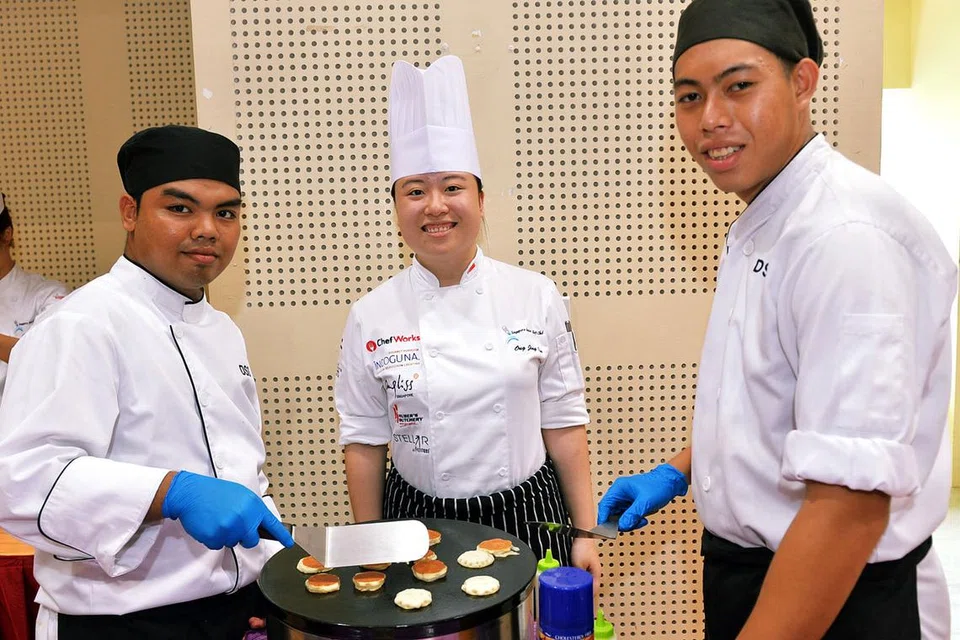 LATIH KEYAKINAN: Encik Nor Safik Bahtiar (kiri) dan rakannya, Encik Chua Zheng Shuang (kanan), merupakan antara pelajar tahun ketiga F&B, Seni Kulinari yang menyediakan hidangan dengan dibantu oleh Presiden Singapore Junior Chefs Club, Cik Ong Jing Qin (tengah). - Foto KHALID BABA