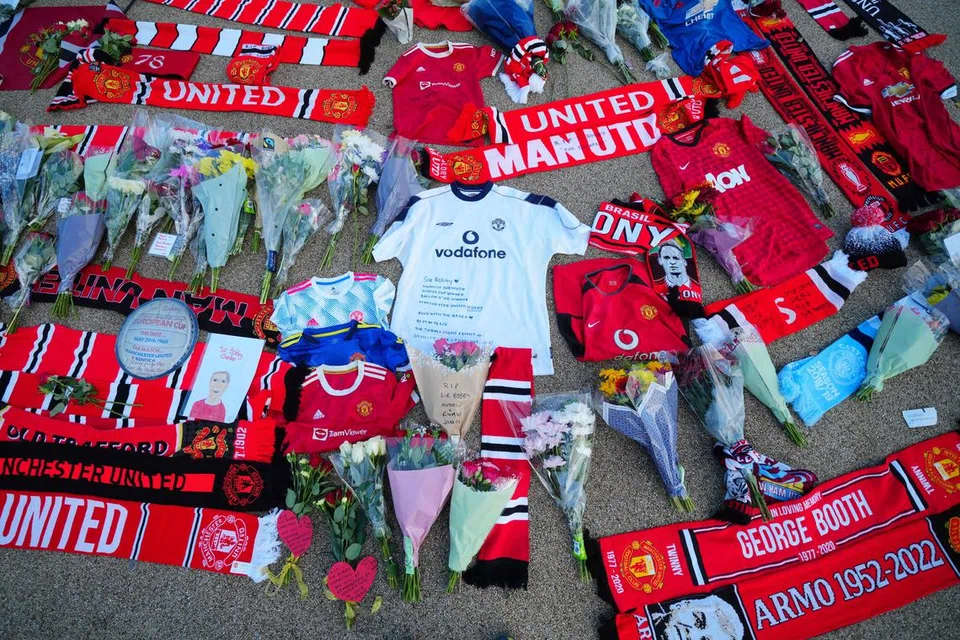 LEGENDA BOLA SEPAK: Kuntuman bunga, selempang dan kemeja-T Manchester United diletakkan di luar stadium Old Trafford di Manchester, berikutan pengumuman pemergian mendiang Sir Bobby Charlton pada Sabtu.