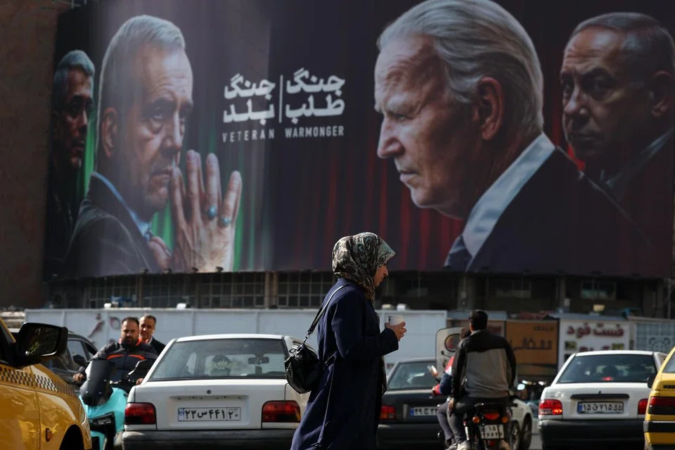 Warga Iran berjalan melewati papan iklan anti-Israel dan anti-Amerika  yang memaparkan gambar Presiden Iran, Encik Masoud Pezeshkian (dua dari kiri) serta Komander Tentera Kor Pengawal Revolusi Islam Iran, Jeneral Mohammad Bagheri (kiri) dengan tajuk ‘Veteran’; dan Presiden Amerika Syarikat, Encik Joe Biden (dua dari kanan) serta Perdana Menteri Israel Encik Benjamin Netanyahu (kanan) dengan tajuk ‘Pencetus Perang’ di Dataran Valiasr, Teheran, Iran, pada 28 Oktober.